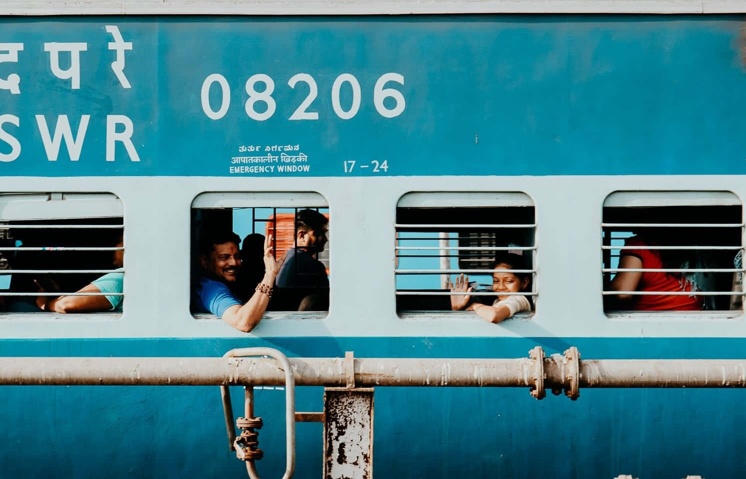 A Blue Train With People Waving Out The Window