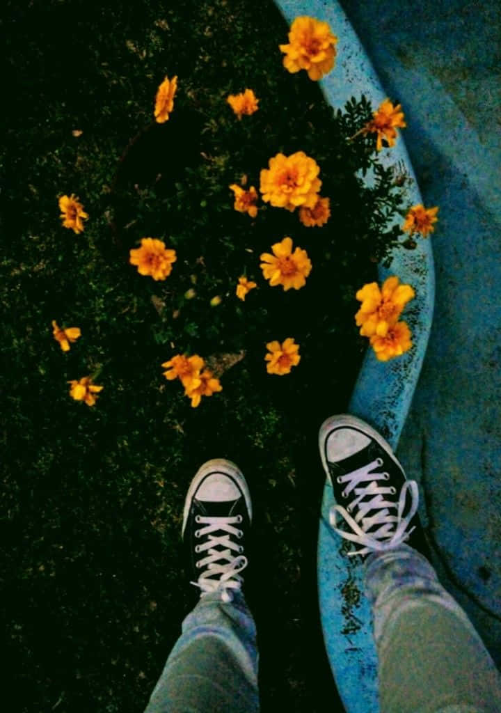 A Person Standing On A Sidewalk With Flowers