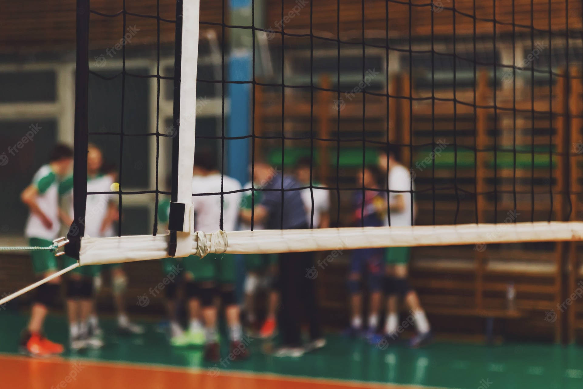 Et volleyball net i en gymnasium med mennesker, der spiller volleyball. Wallpaper