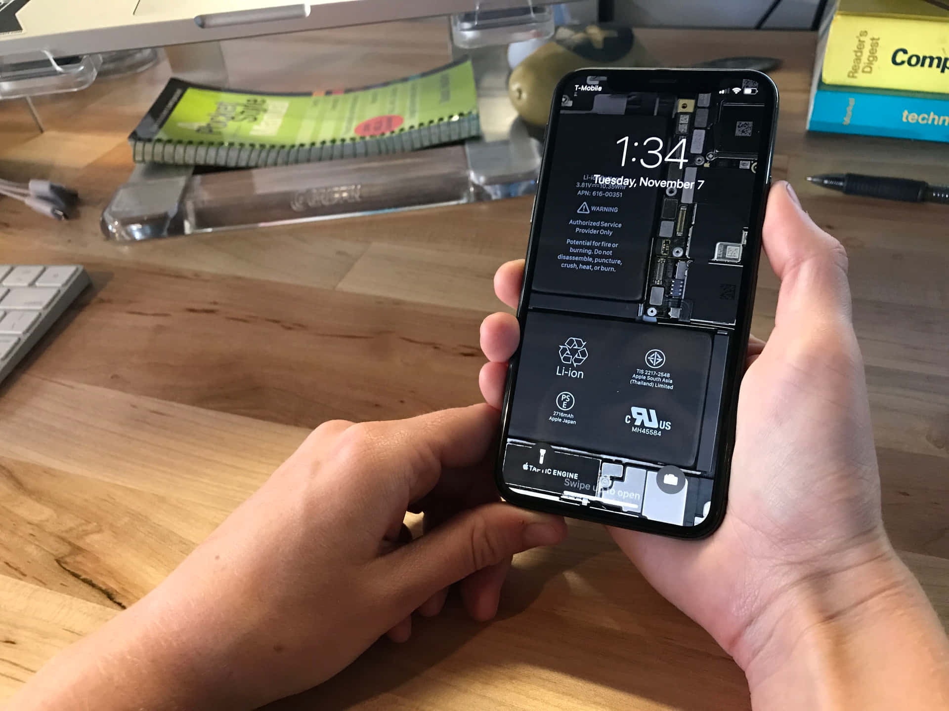 A Person Holding Up An Iphone X On A Desk Wallpaper