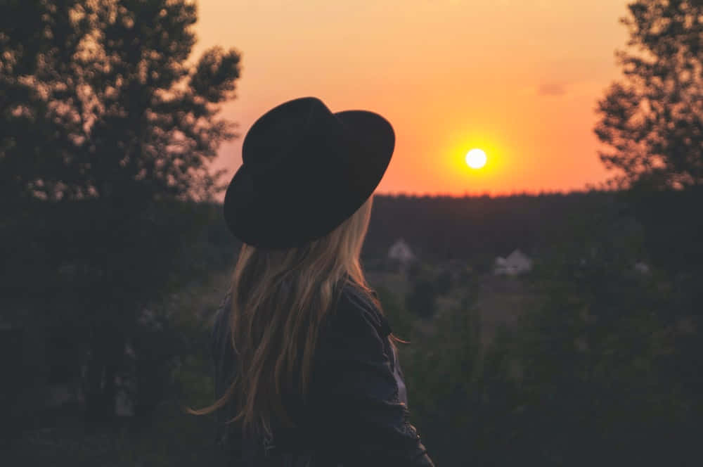 Einefrau Mit Hut, Die Den Sonnenuntergang Betrachtet.