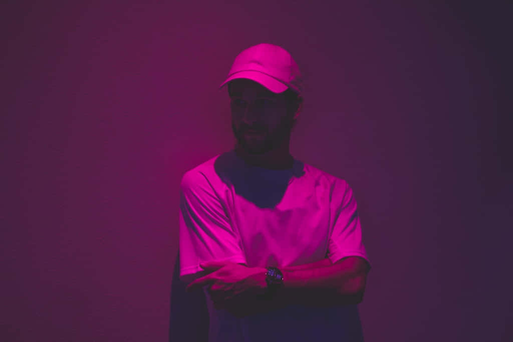 A Man In A Hat And A Cap Standing In Front Of A Purple Wall