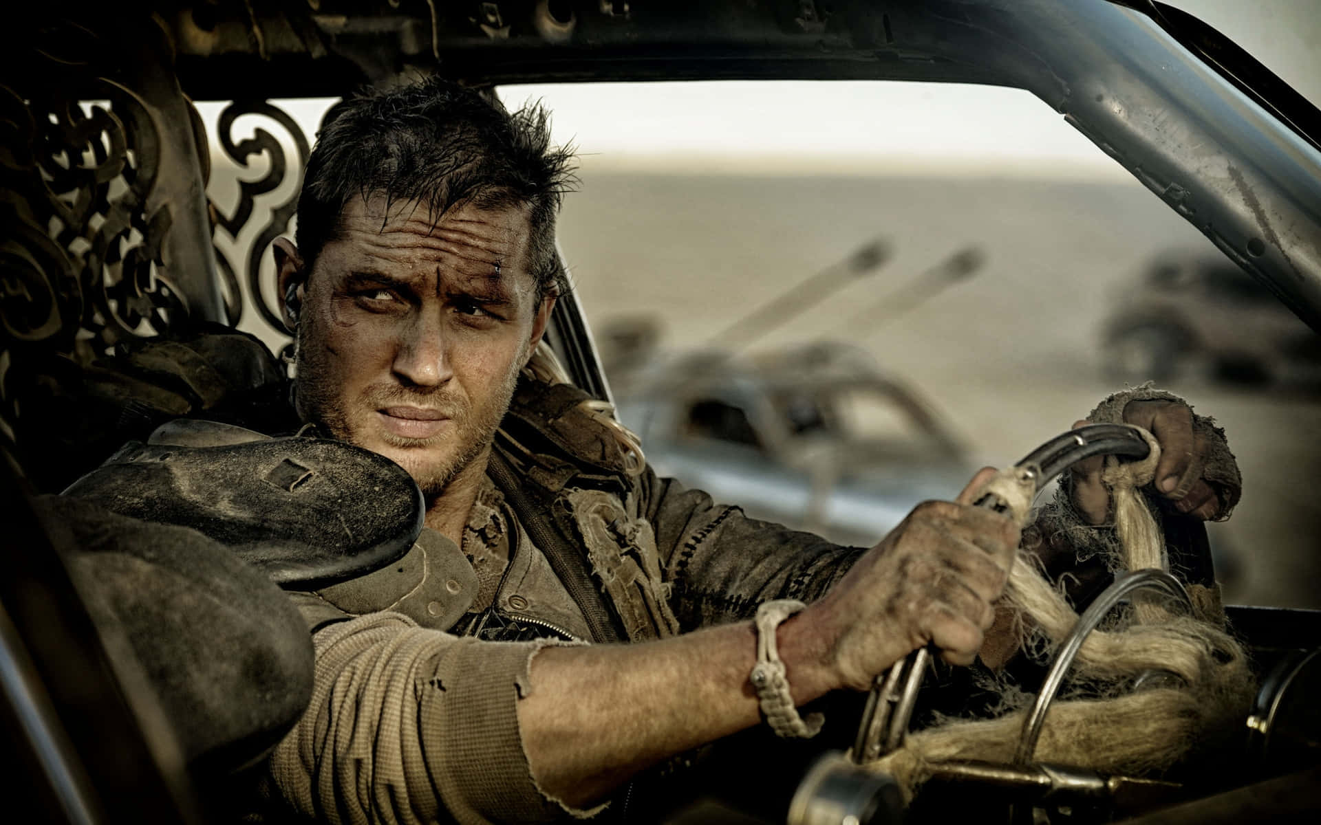 Intense Stare Of Max Against Sun-baked Desert Backdrop In Mad Max Fury Road Wallpaper
