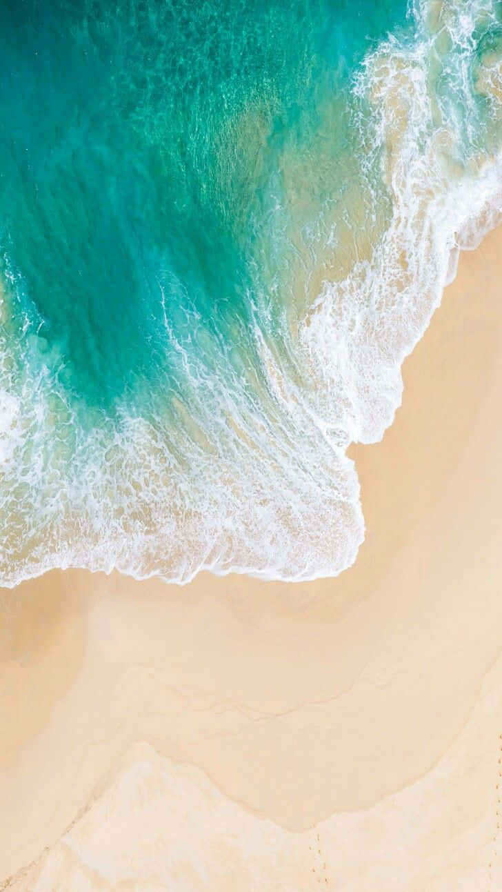 Aerial View Of A Beach With Waves And Footprints Wallpaper