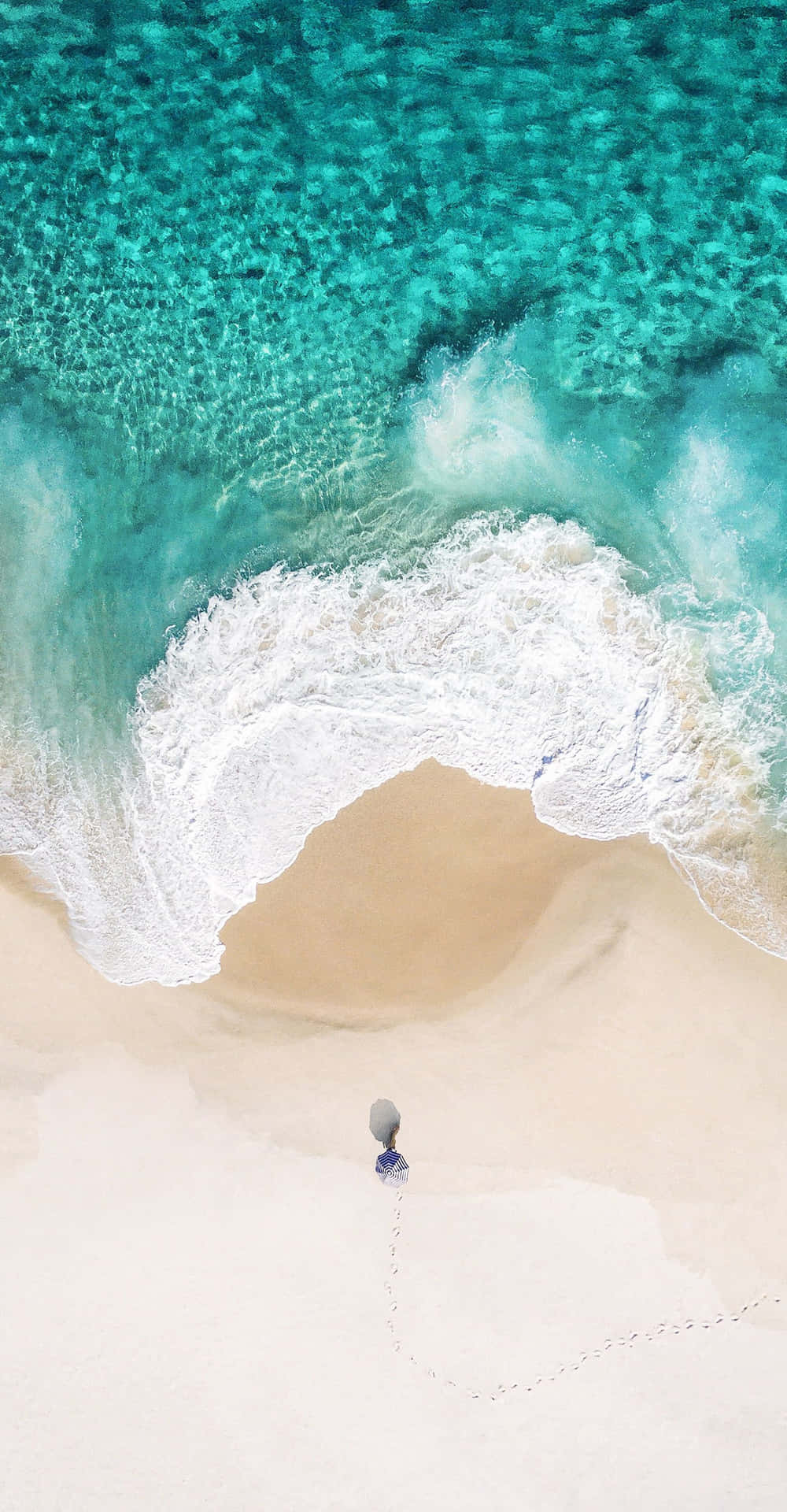 En person står på en strand med en parasol. Wallpaper