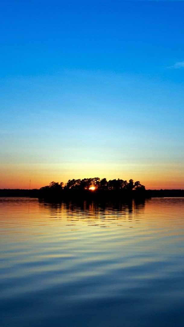 En solnedgang over en sø med træer på den. Wallpaper