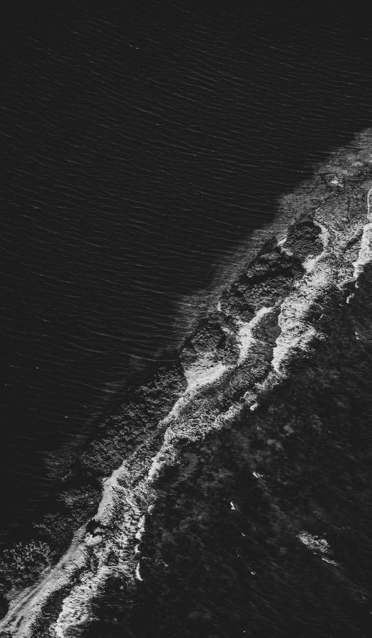 Et sort og hvidt foto af en strand med bølger, der kolliderer Wallpaper