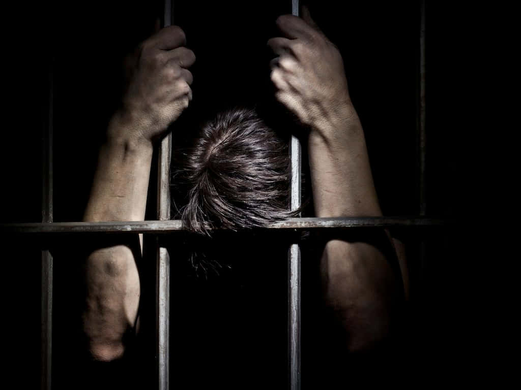 A Man Is Holding His Head Up In A Jail Cell