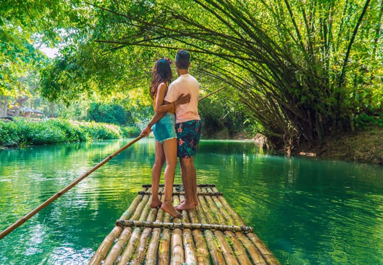 A Couple Standing On A Bamboo Raft In A River