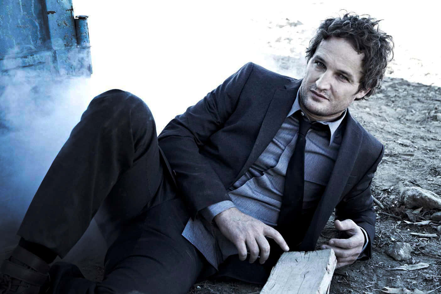 Jason Clarke Suited Upand Seated Outdoors Wallpaper