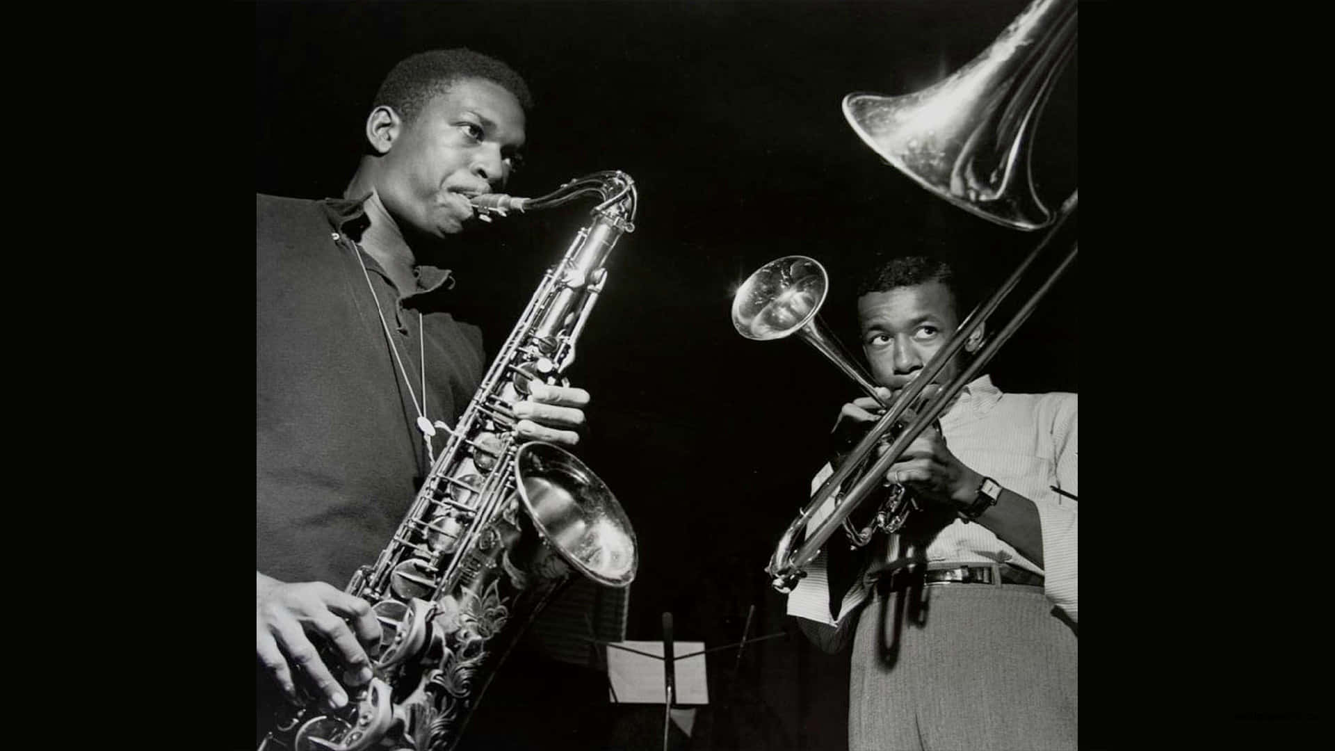 Two Men Playing Saxophones In A Black And White Photo