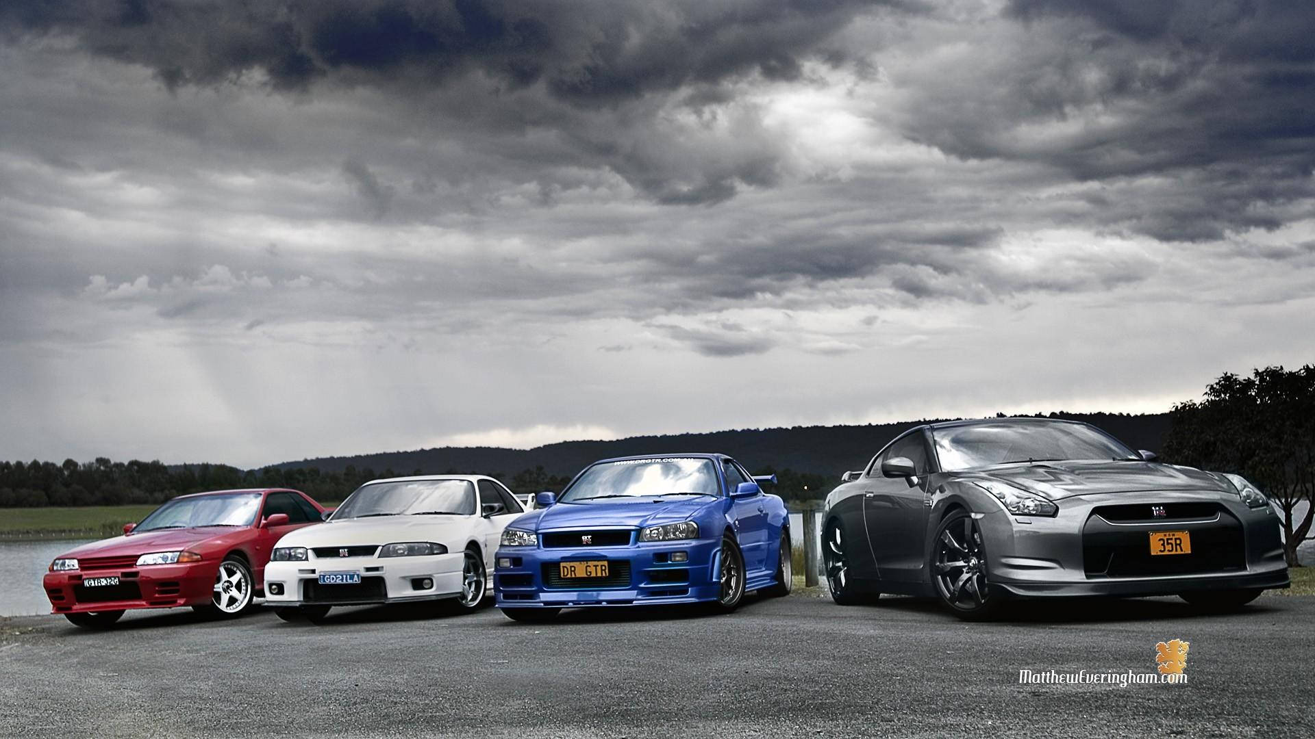 A display of illustrious JDM performance cars against a cloudy sky Wallpaper