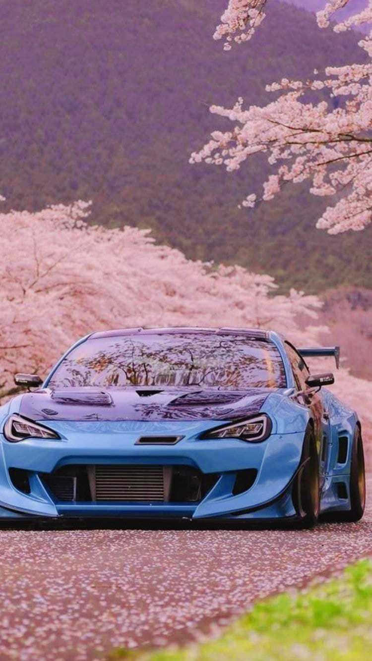 A Blue Sports Car Parked In Front Of A Cherry Tree