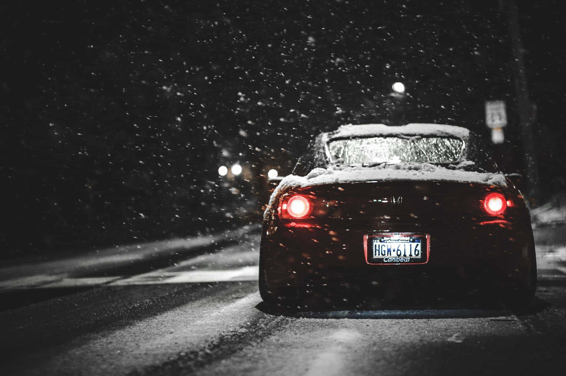 A Red Car Driving Down A Snowy Street At Night Wallpaper