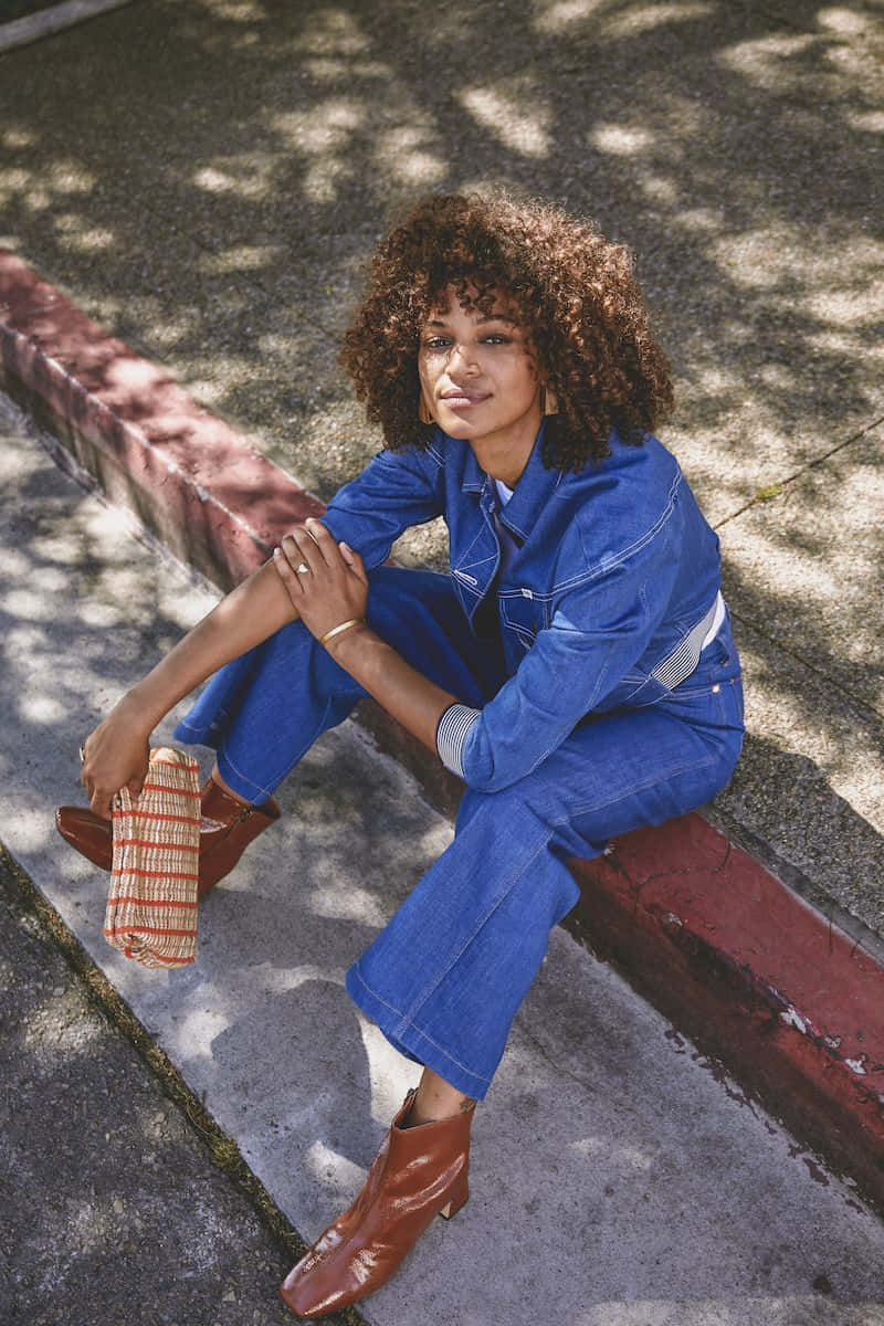 A Woman In Denim Overalls Sitting On The Curb