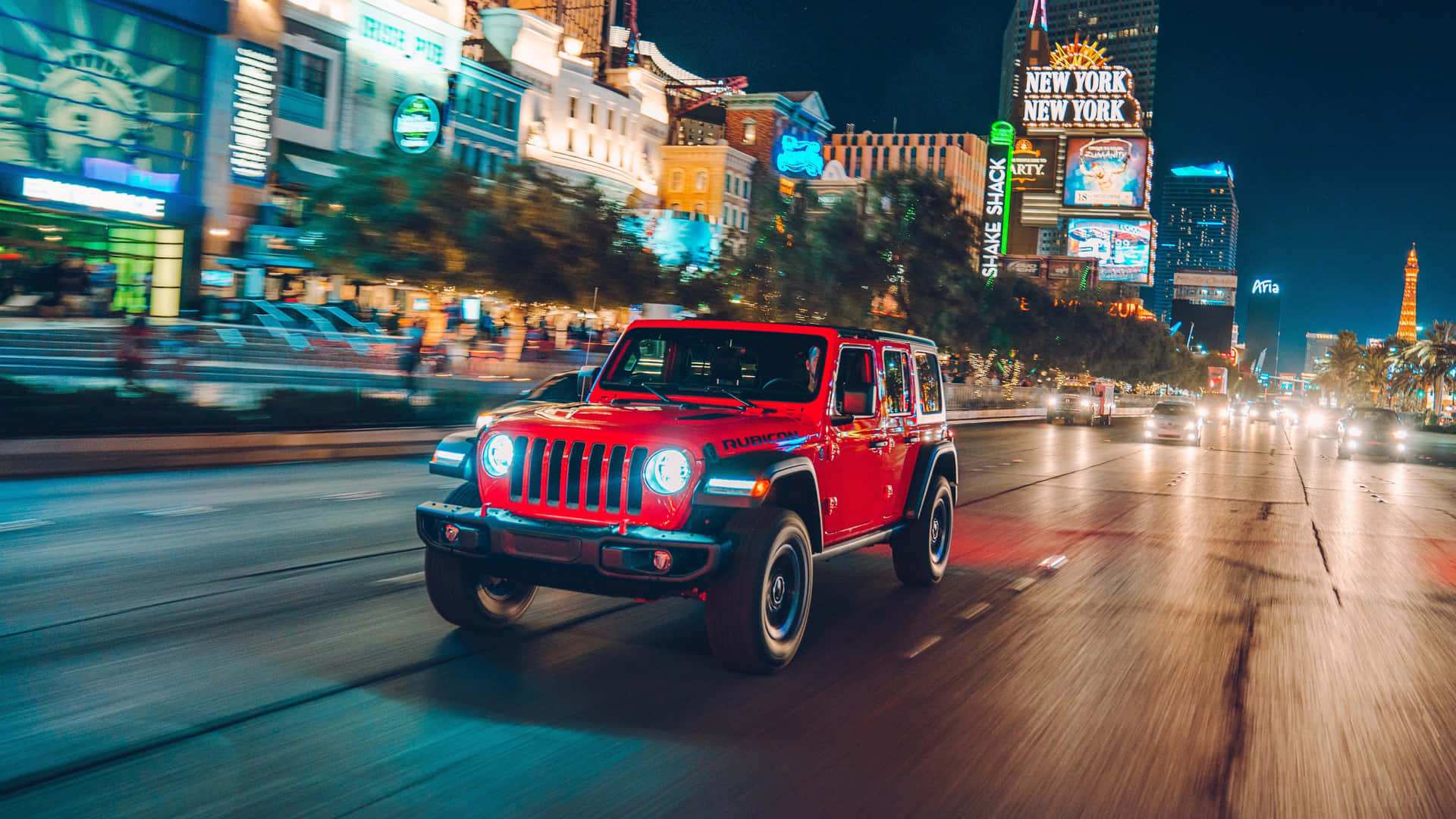 A Red Jeep Wrangler Driving Down A City Street At Night