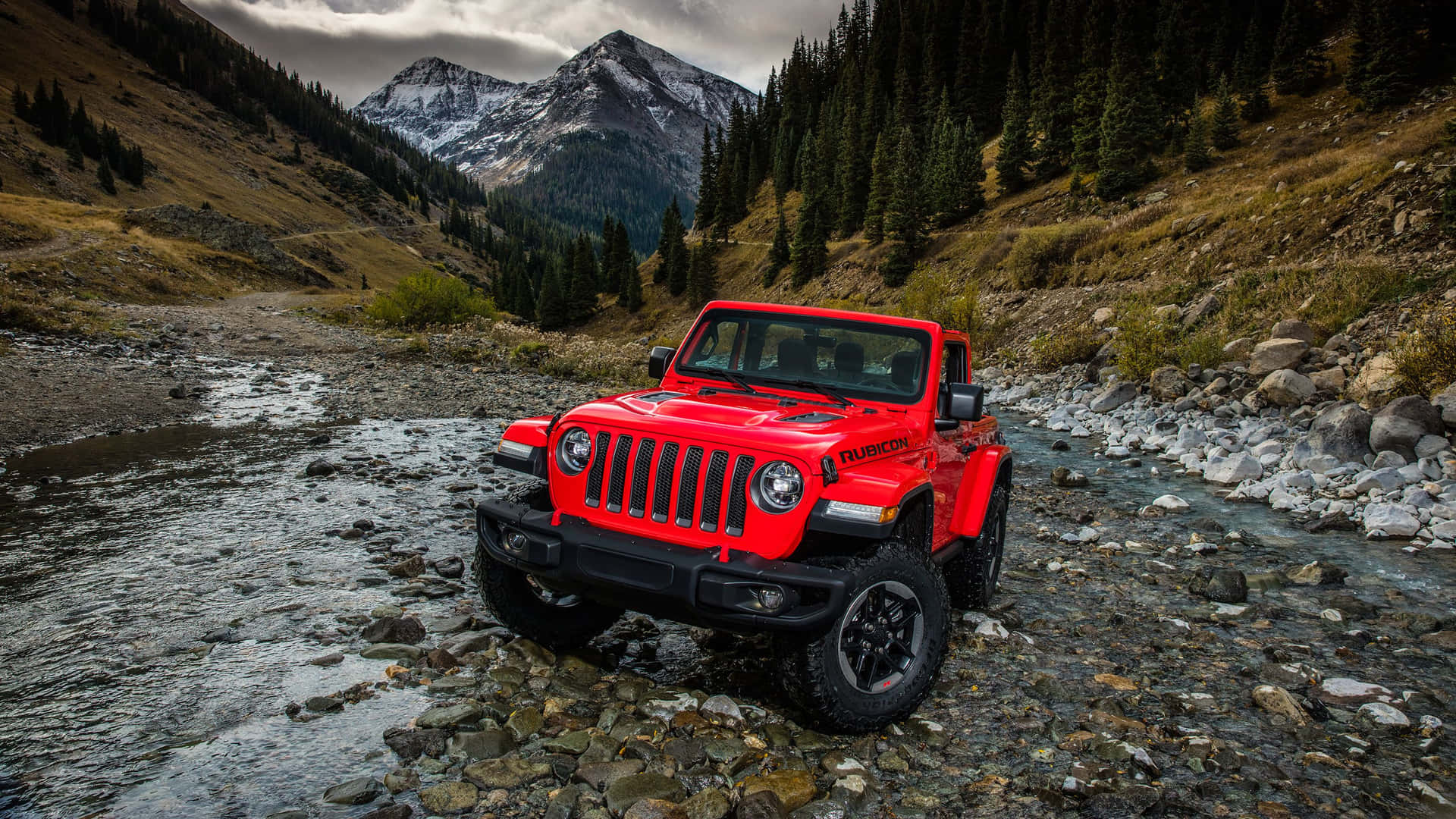A Red Jeep Is Parked In A Stream In The Mountains
