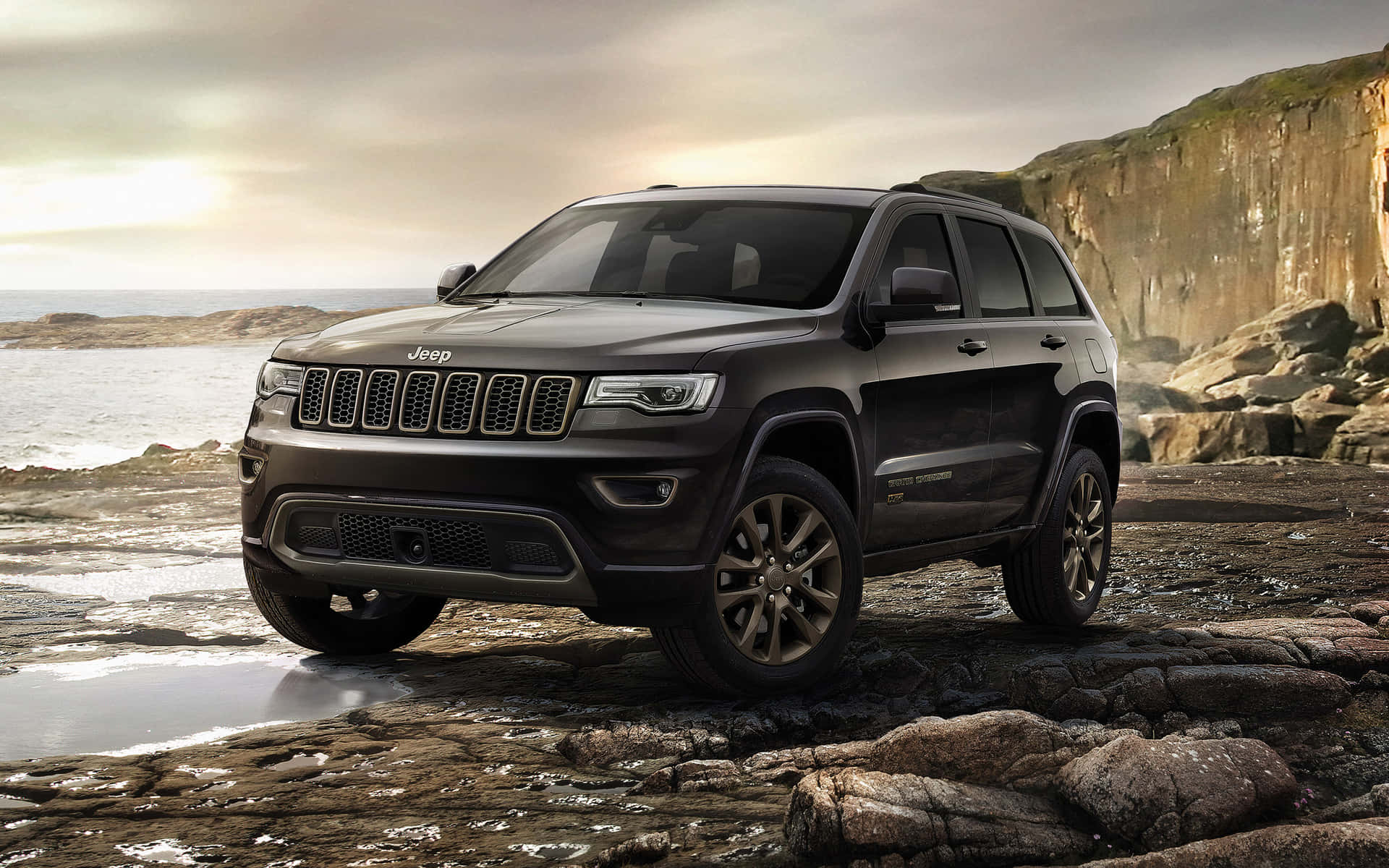 The New Jeep Grand Cherokee Is Parked On A Rocky Beach Wallpaper