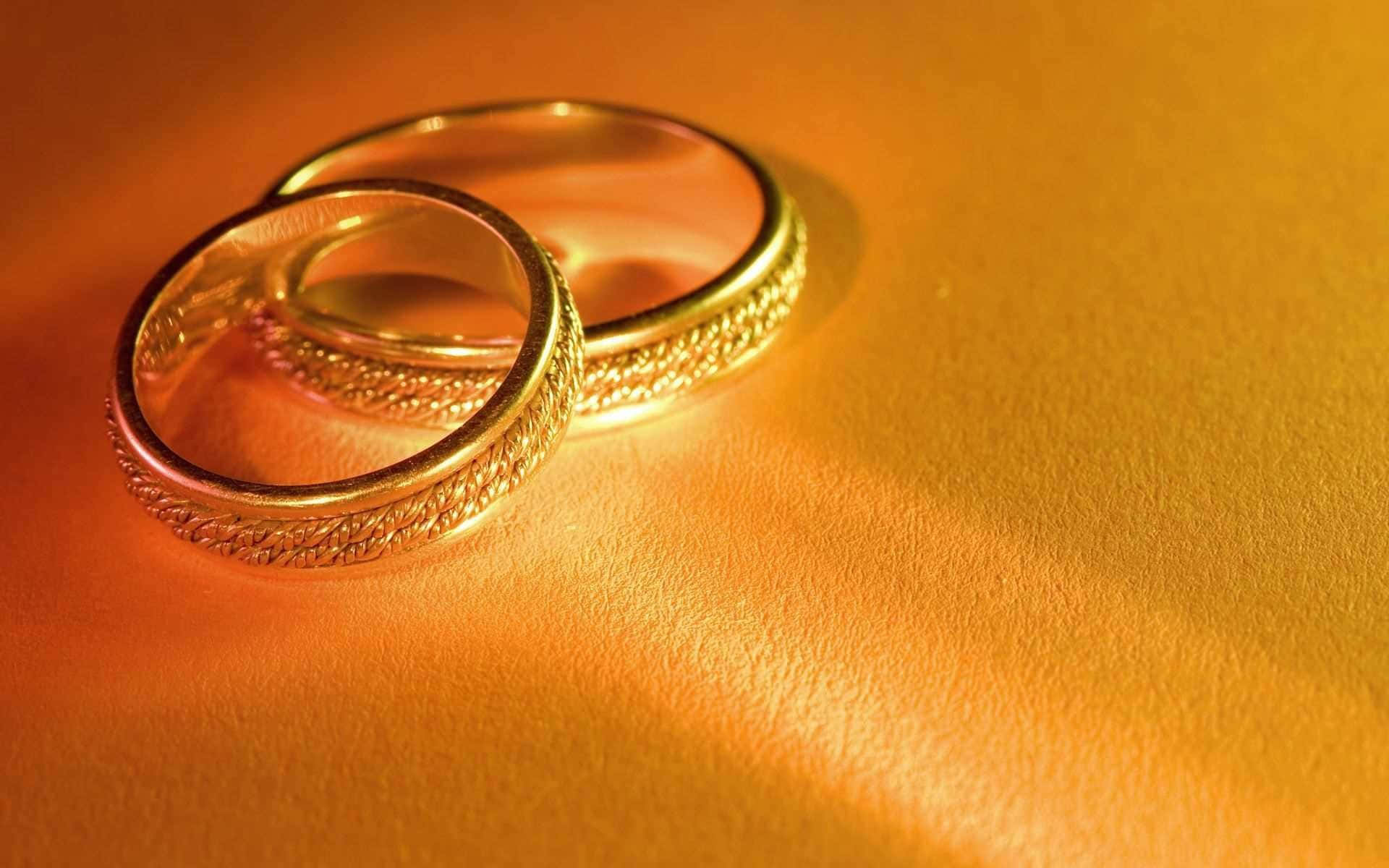 Two Gold Wedding Rings On A Yellow Surface