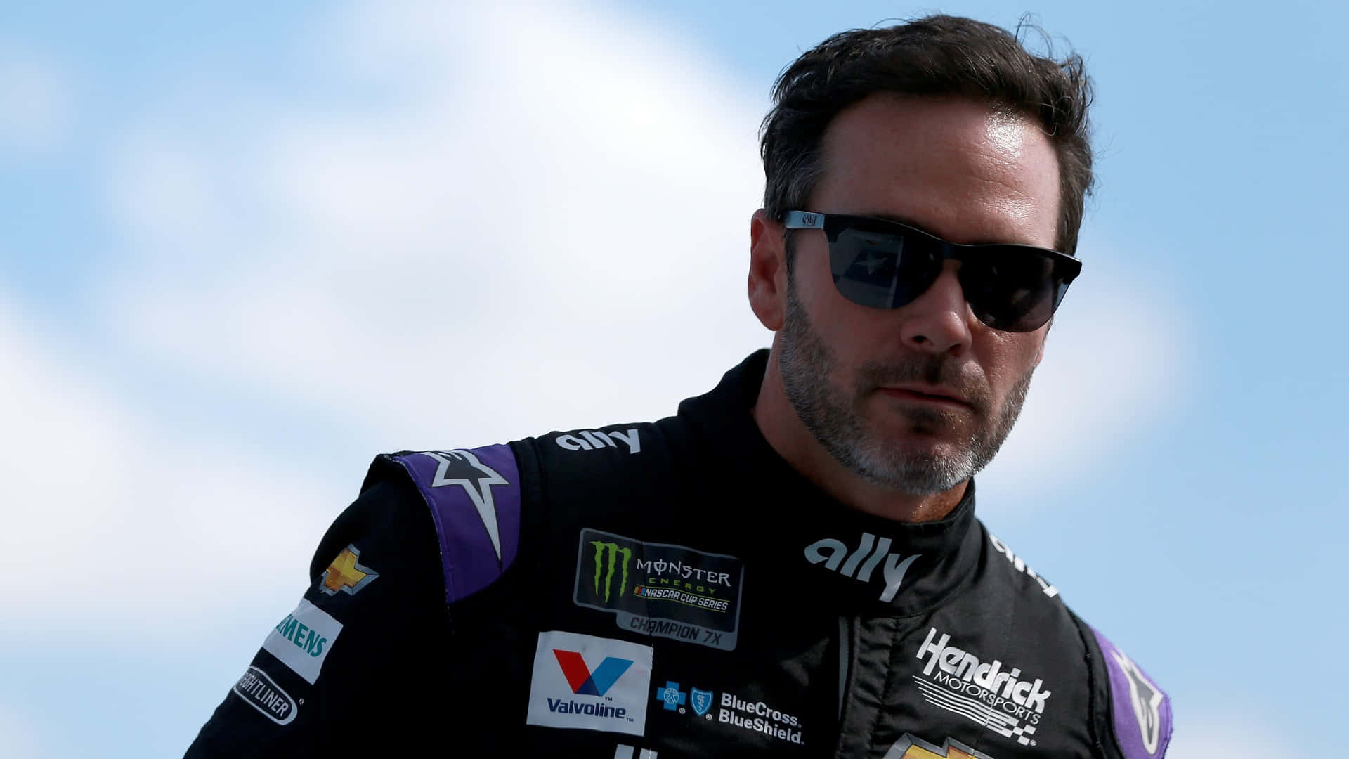Jimmie Johnson in his racing gear with his car on the track Wallpaper