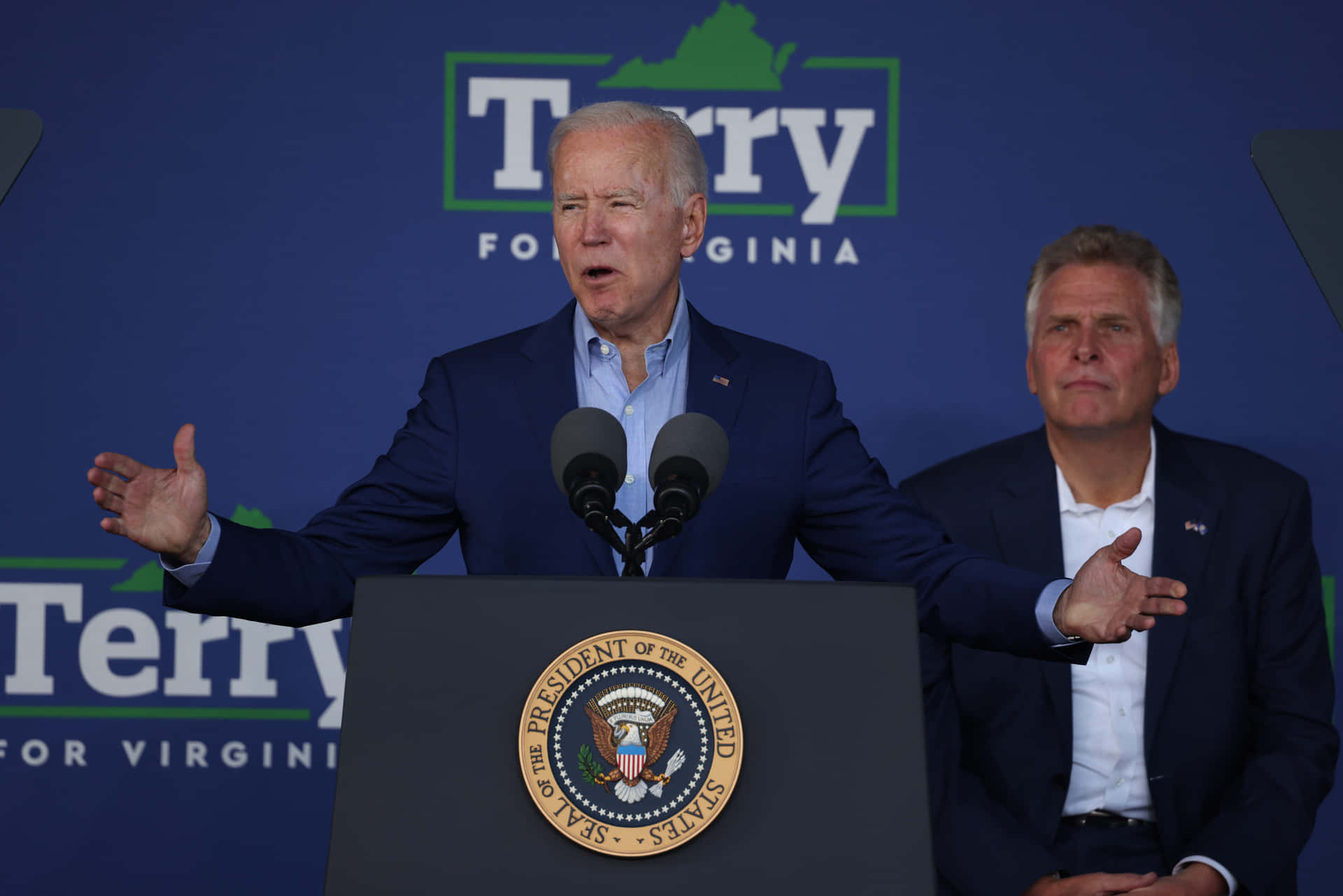 Joe Biden Delivering A Speech With Terry McAuliffe Behind Him Wallpaper
