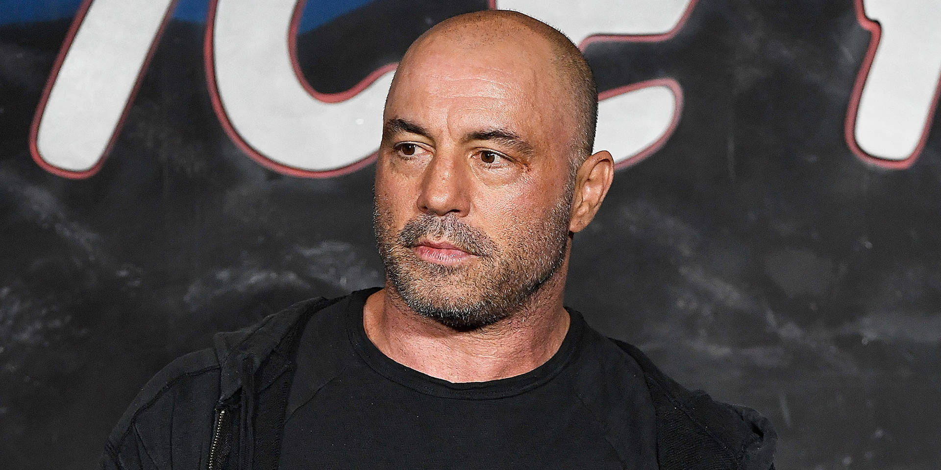 Joe Rogan Engaged in a Lively Conversation at a Public Event Wallpaper