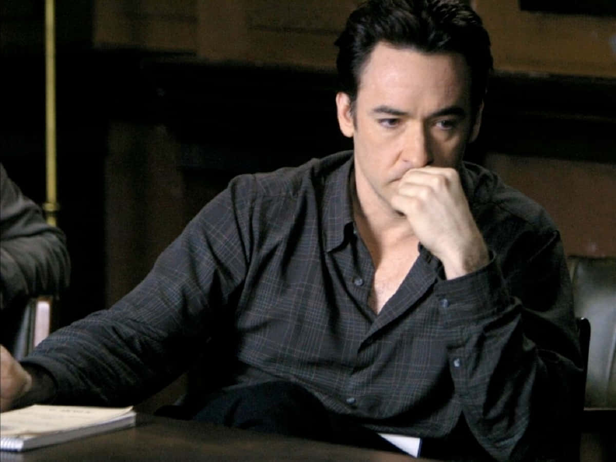 John Cusack strikes a casual pose in black attire against a blurred cityscape Wallpaper