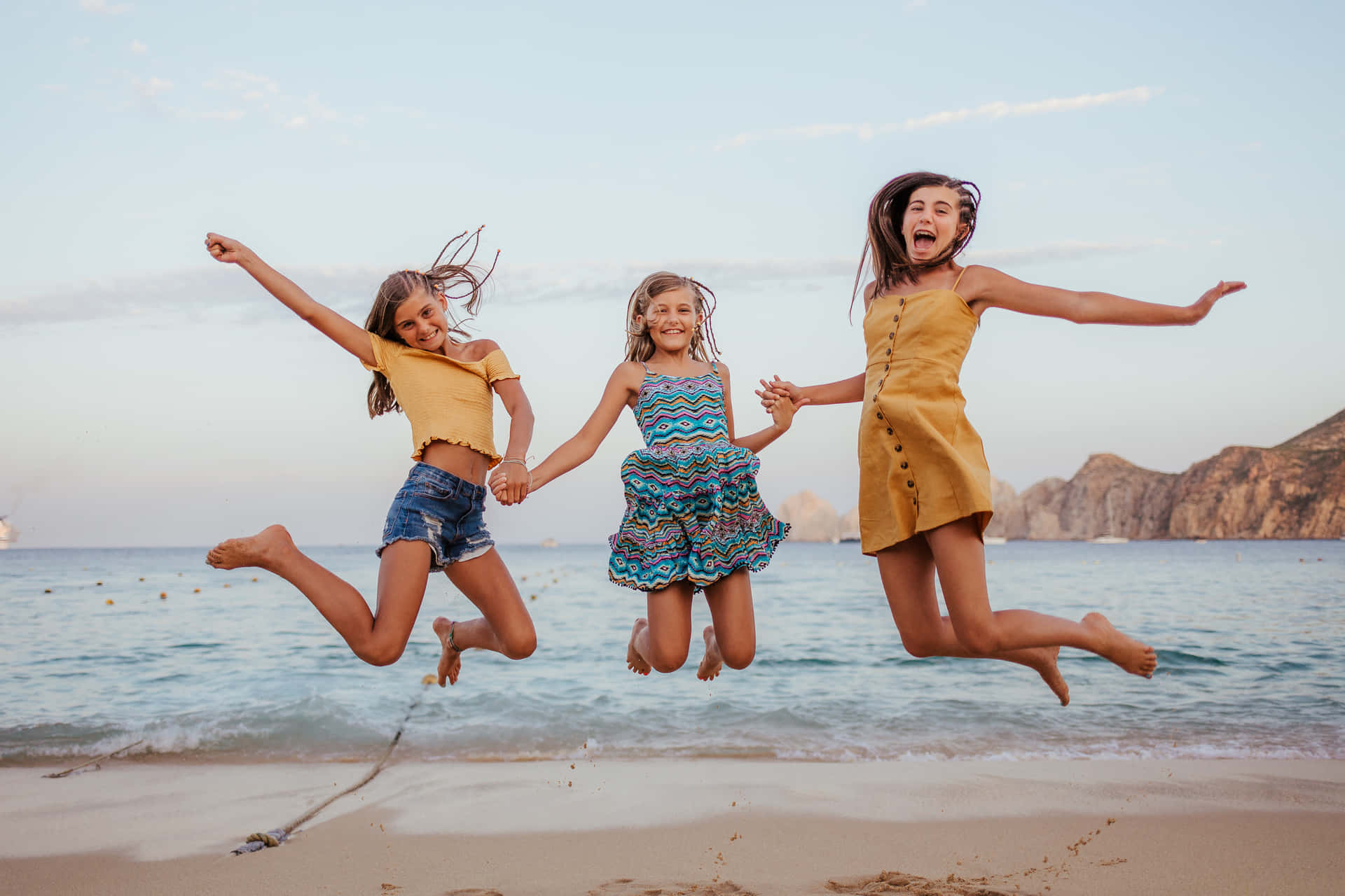 Joyful Sisters Jumpingon Beach Wallpaper