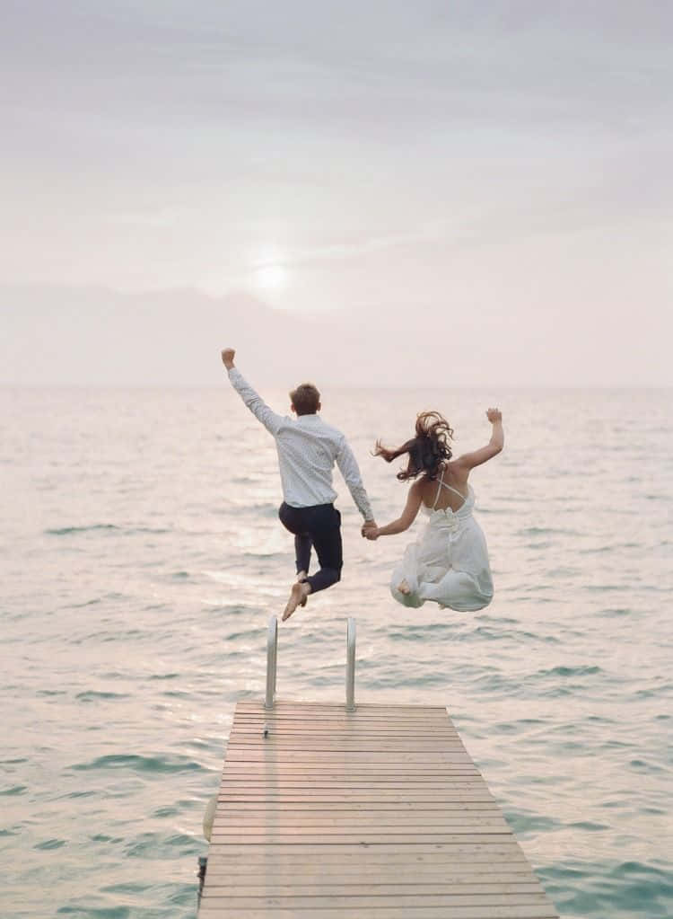 A Bride And Groom Jumping Off A Dock