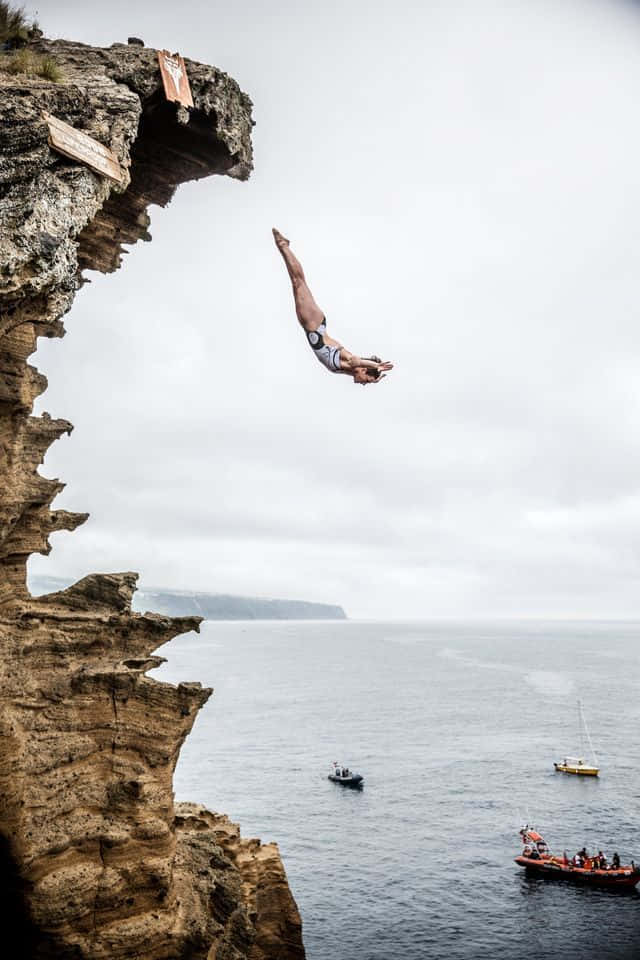 A Man Diving Off A Cliff Into The Ocean