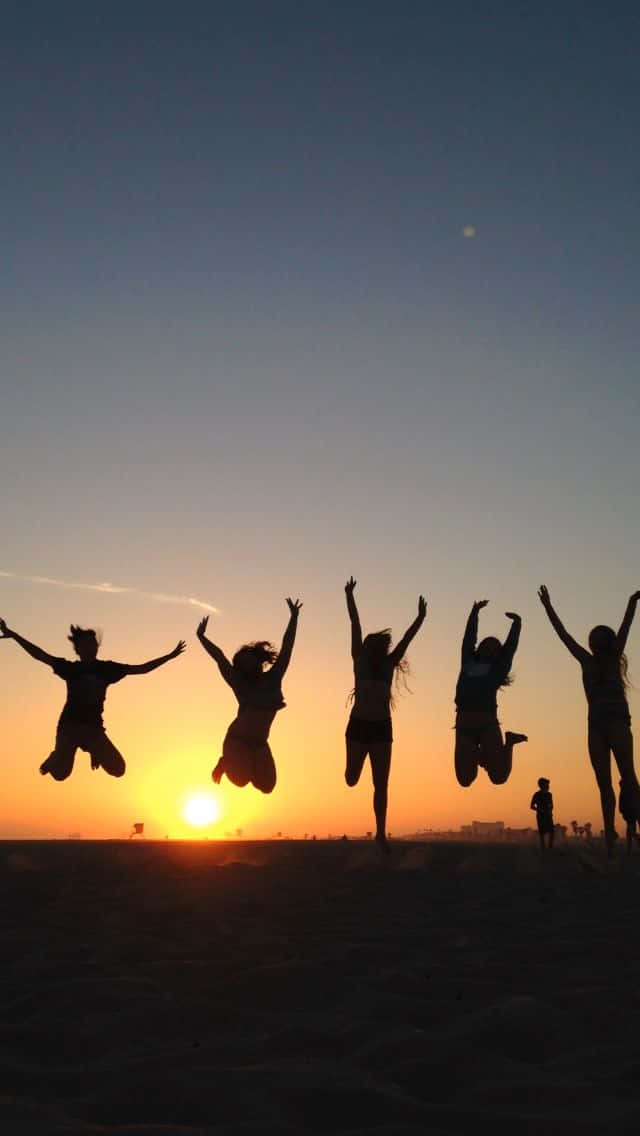 A Group Of People Jumping In The Air At Sunset