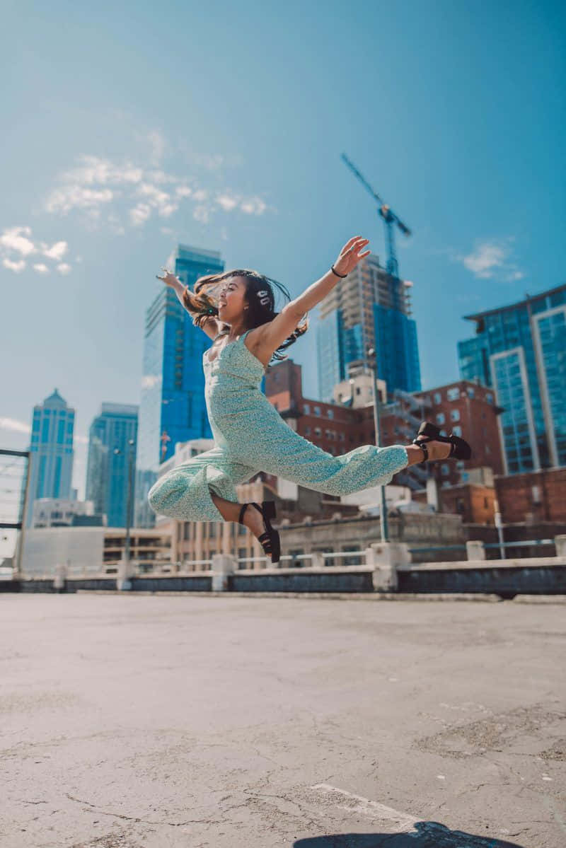 A Young Woman Jumping In The Air In Front Of A City