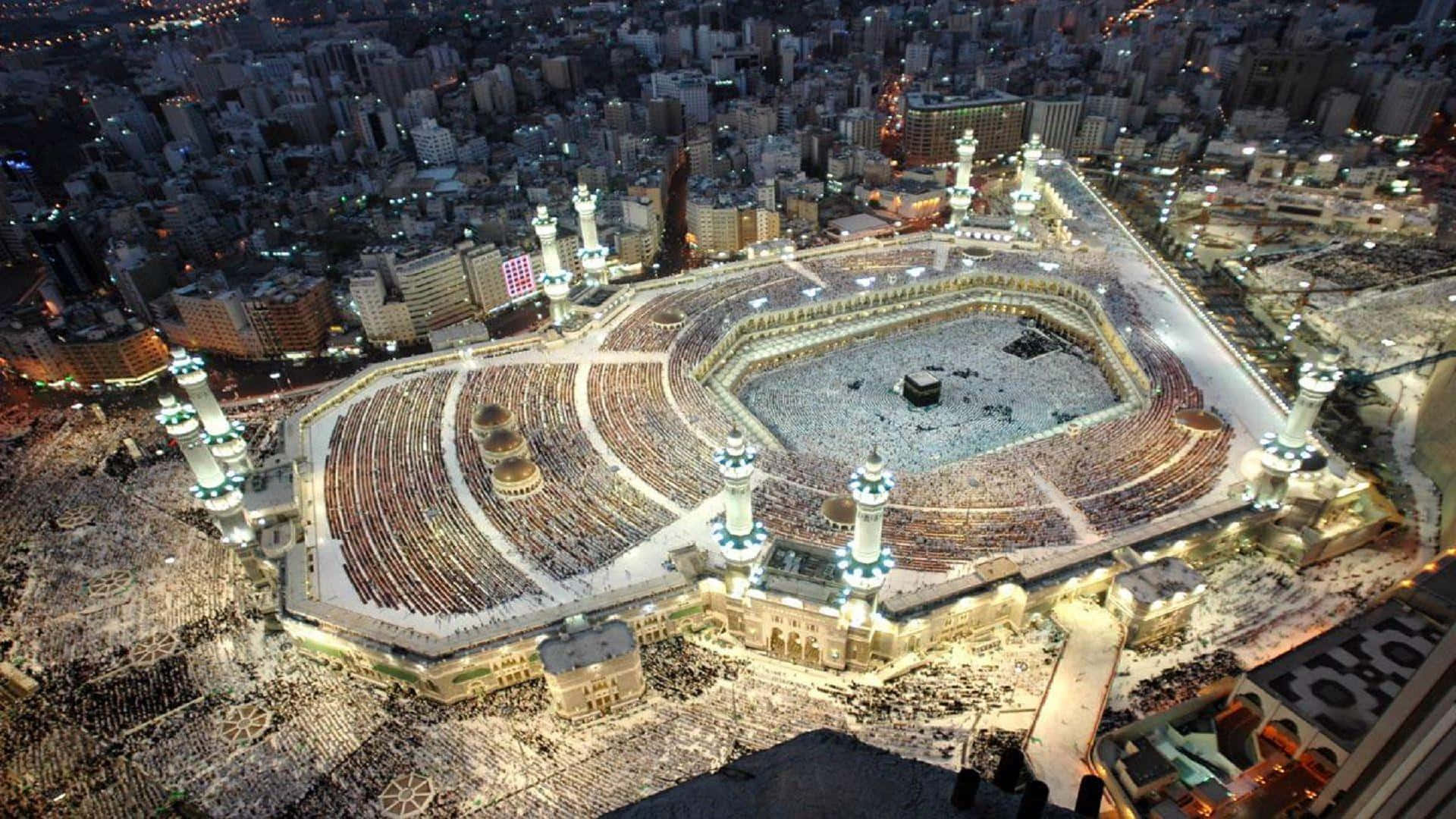 Download The Kaaba At Night With People Around It | Wallpapers.com