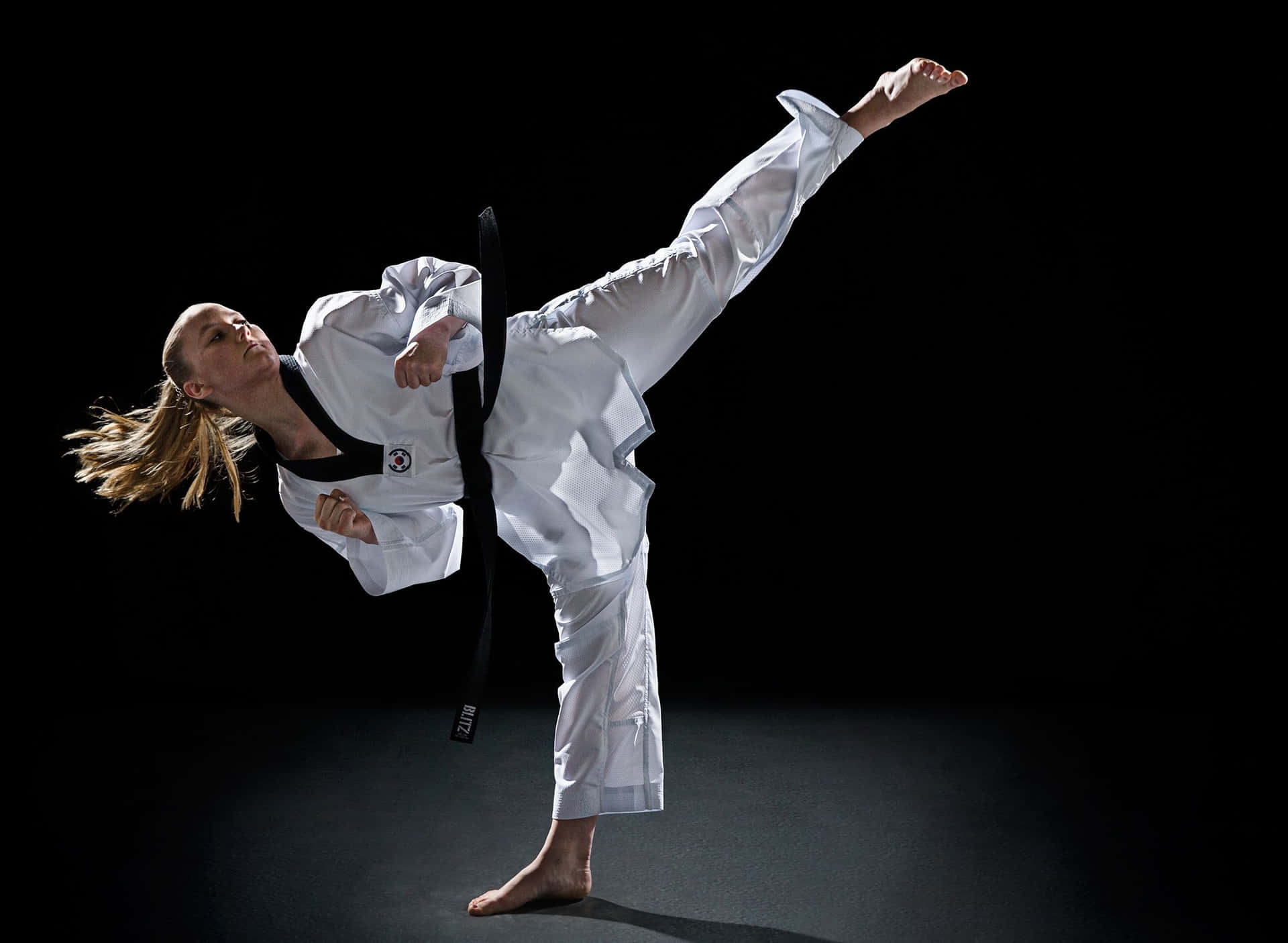 A Woman In A White Karate Outfit Doing A Kick