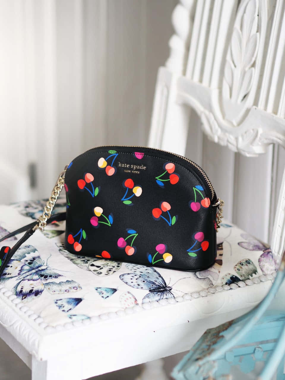 A Black Purse With Cherries On It Sits On A Chair