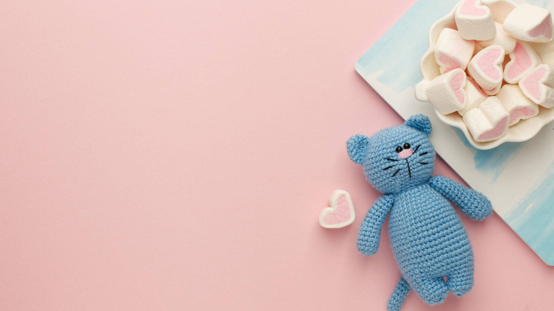 A Blue Crochet Cat With Marshmallows On A Pink Background Wallpaper