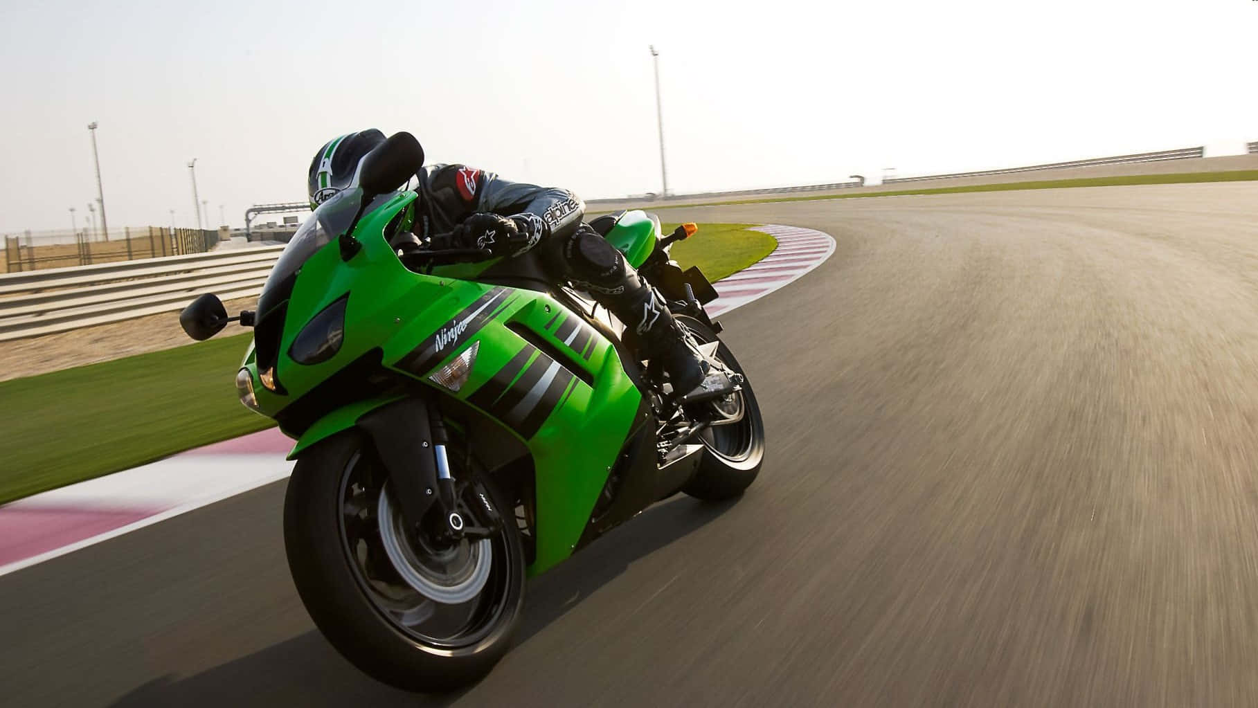 A Green Motorcycle Is Racing Down A Track Wallpaper