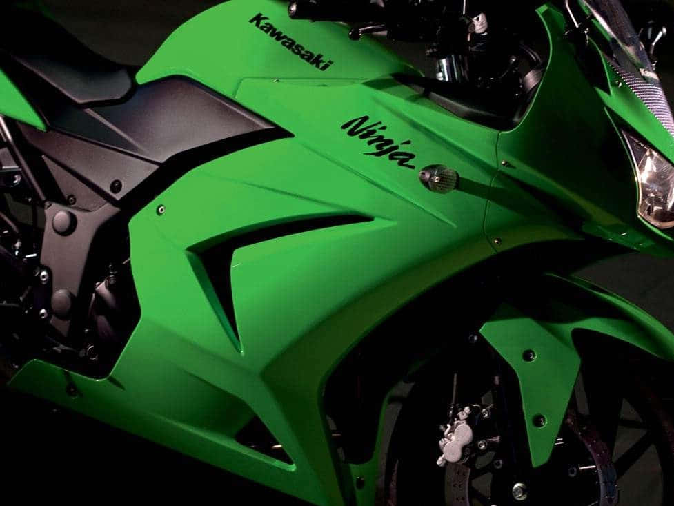 A Green Motorcycle Is Parked In A Dark Room Wallpaper