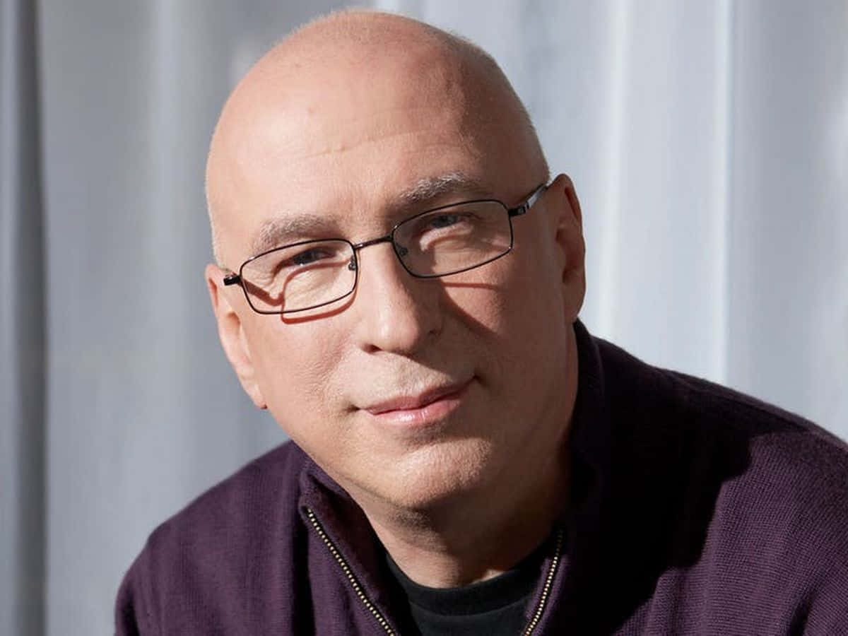 A Bald Man In Glasses Is Sitting In Front Of A Curtain Wallpaper