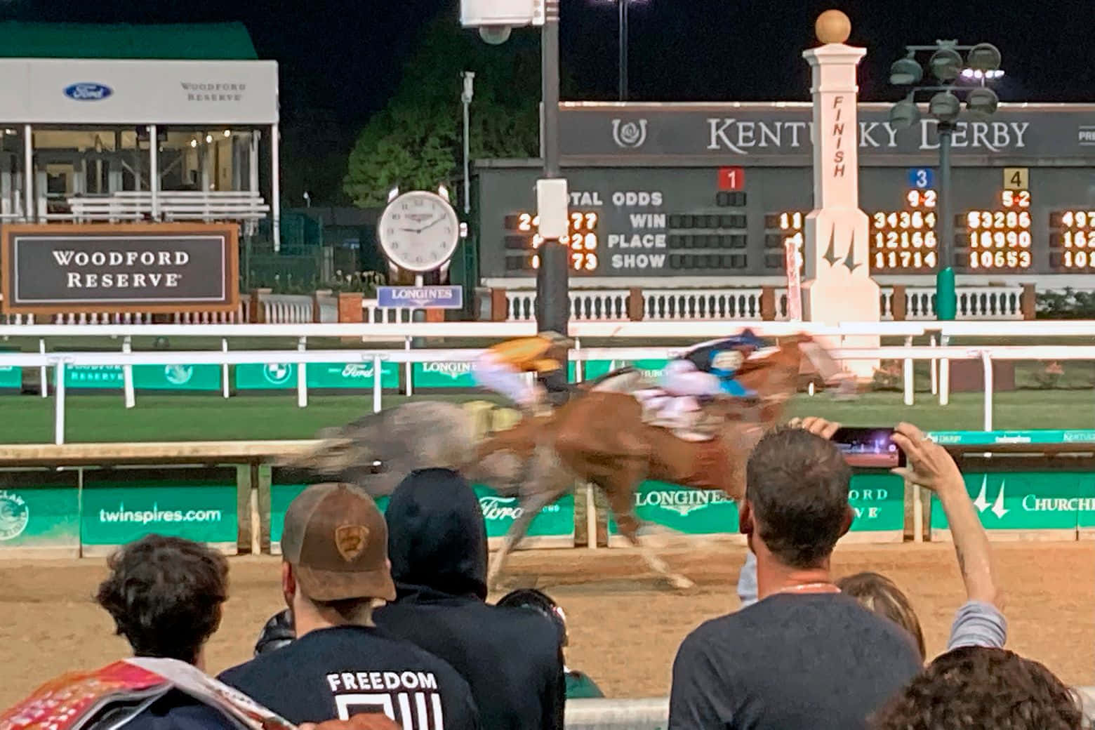 A Crowd Watches A Horse Race At Night