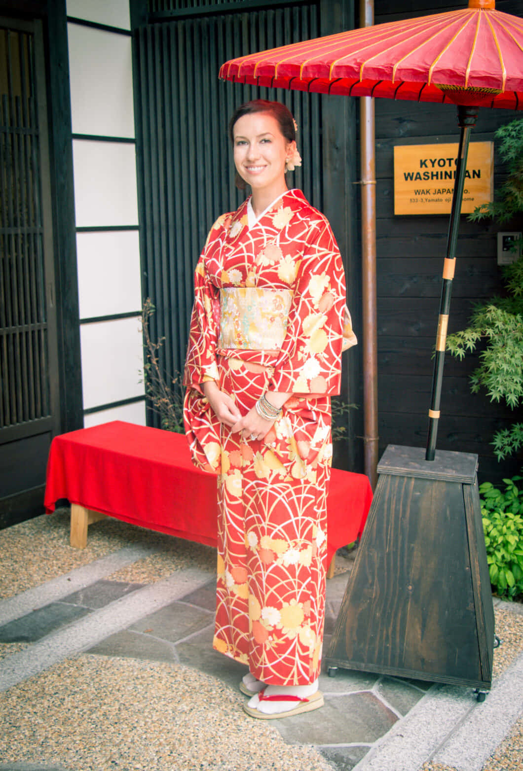 A Woman In A Red And Yellow Kimono Standing Under An Umbrella