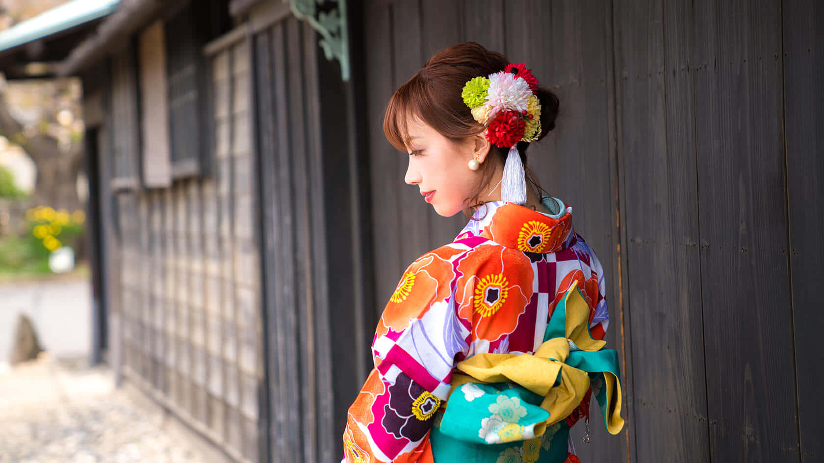 A Woman In A Kimono Is Standing Next To A Wooden Building