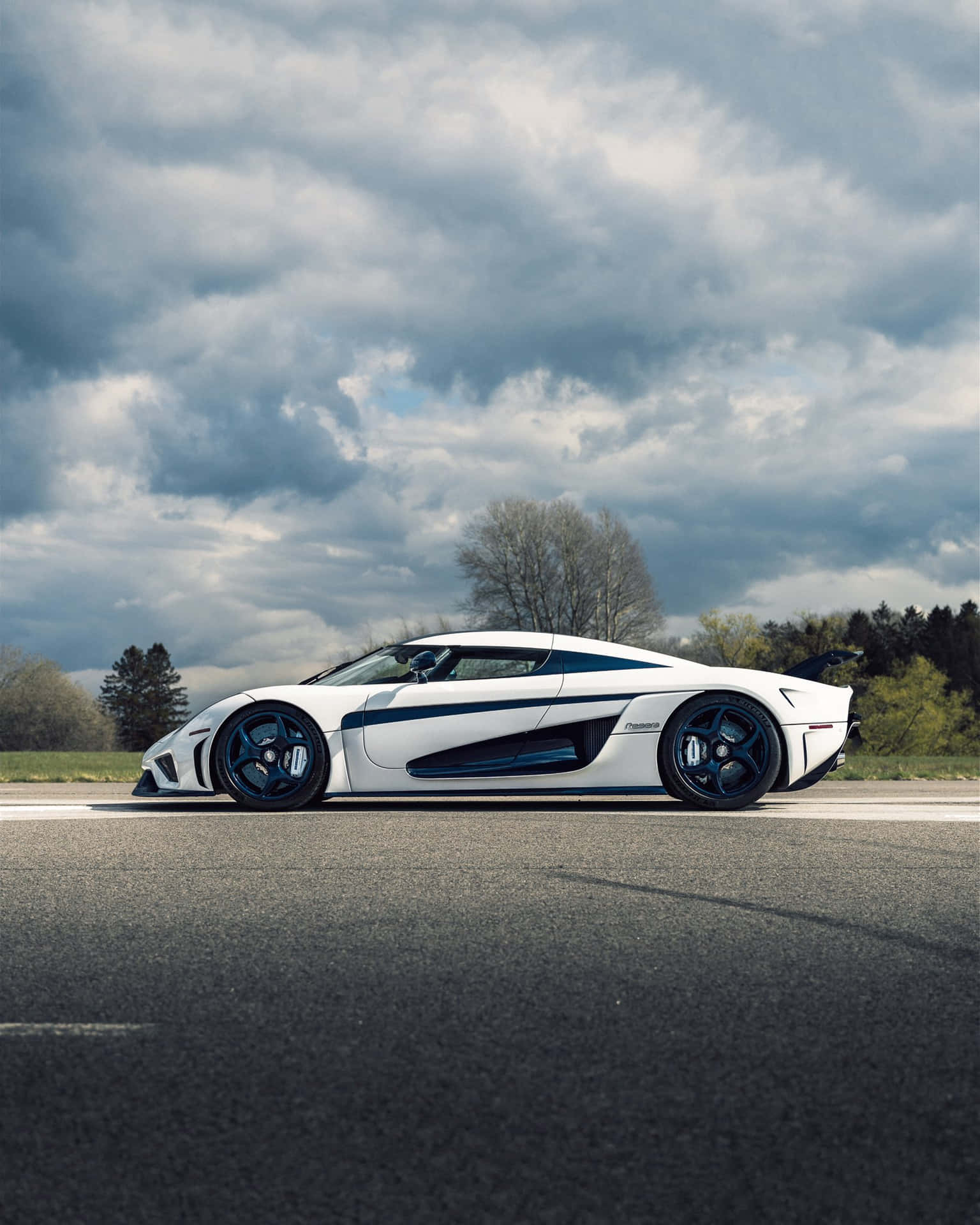 A White And Blue Sports Car Is Driving Down The Road Wallpaper