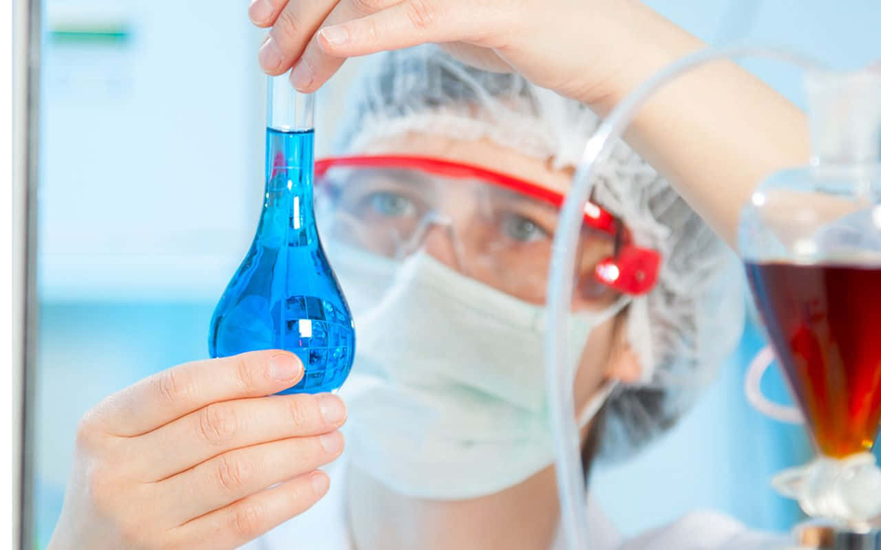 A Scientist Is Holding A Blue Liquid In A Glass