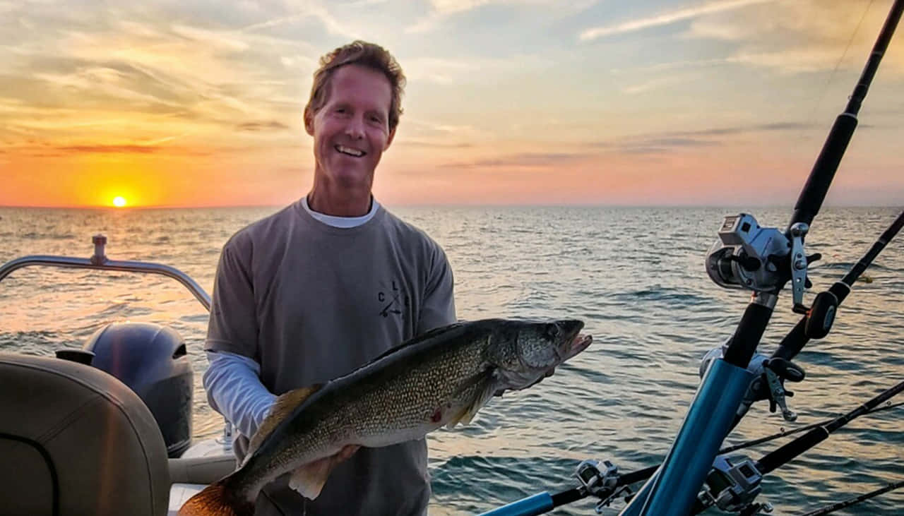 A Man Holding A Fish On A Boat At Sunset