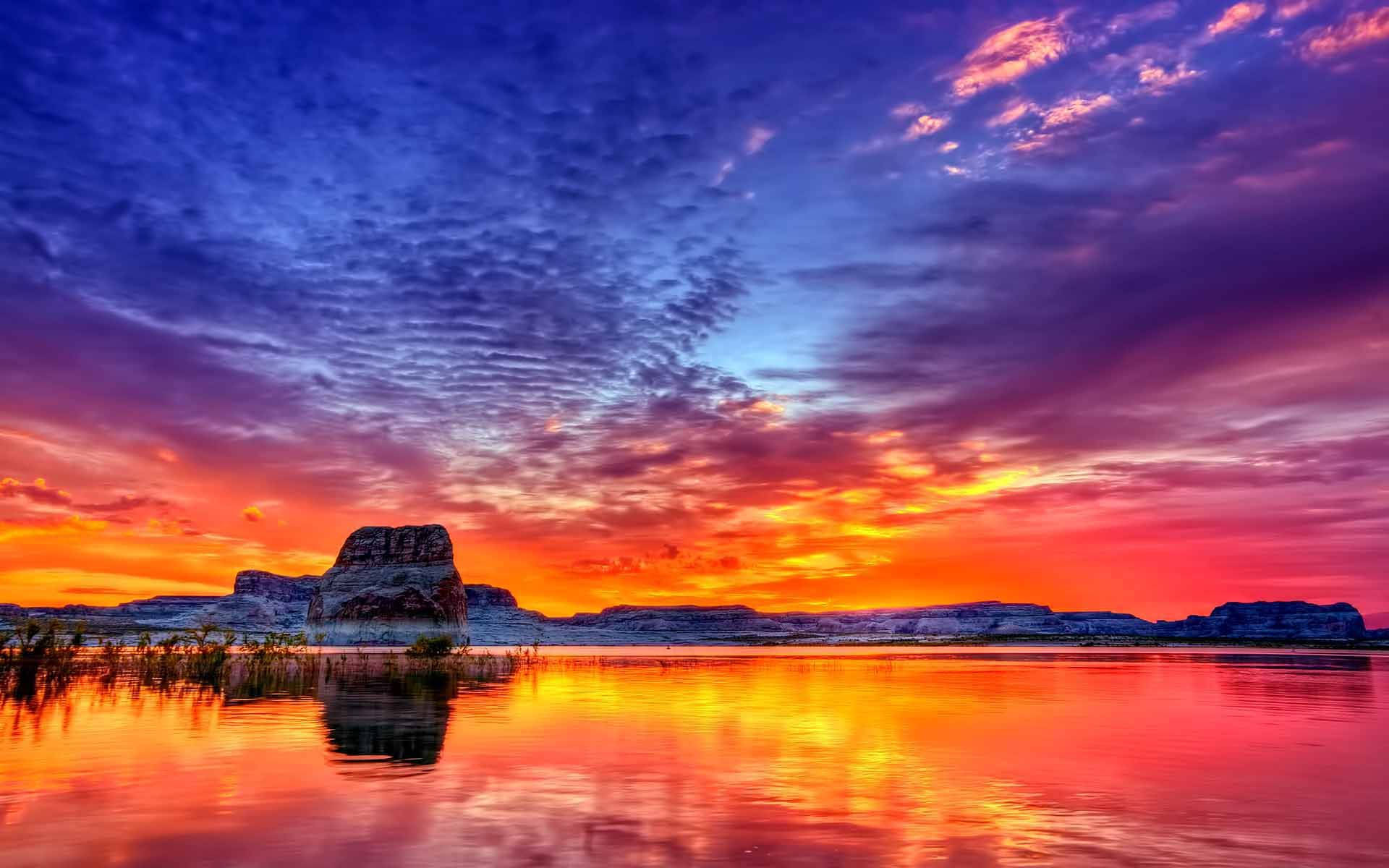 A tranquil lake is illuminated by vivid colors at sunset. Wallpaper