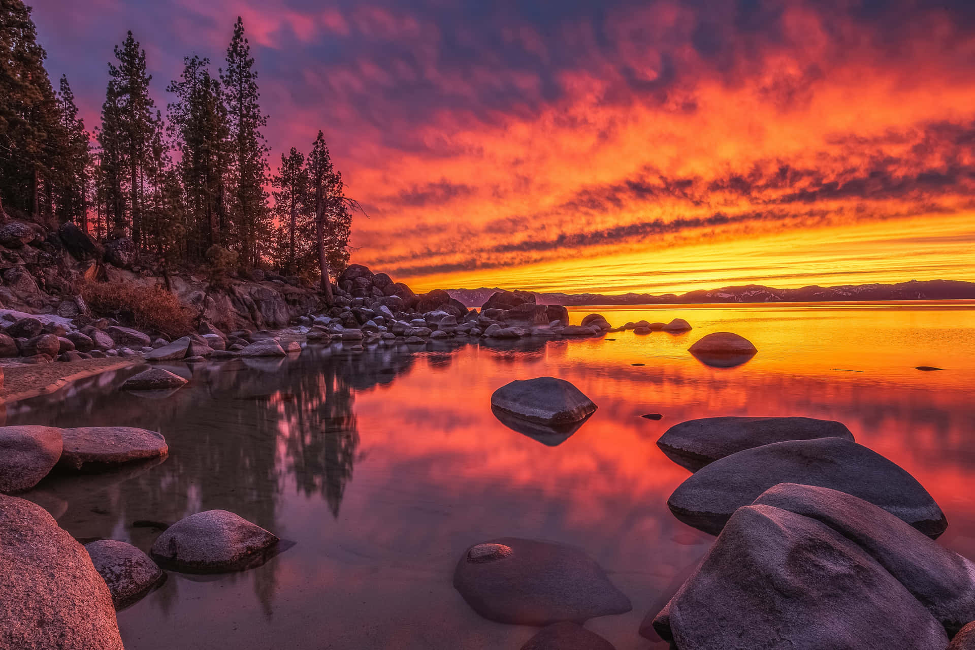 A Sunset Over A Lake With Rocks And Trees Wallpaper