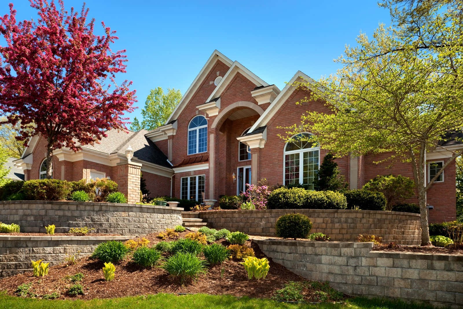 A Brick Home With A Stone Driveway And Landscaping
