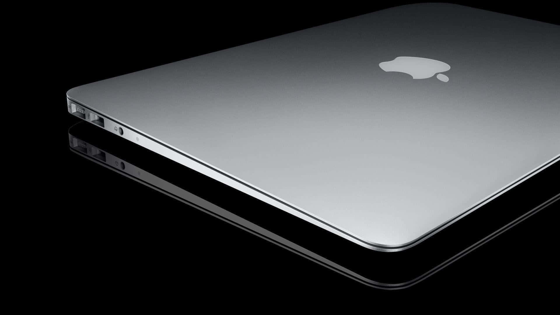 Et sølv Macbook Pro vises på en sort overflade. Wallpaper