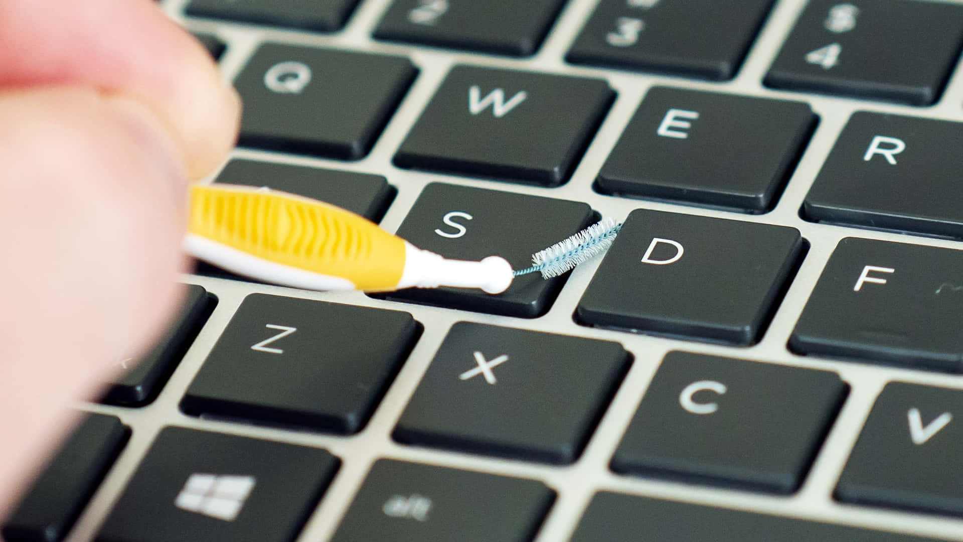 En person bruger en tandbørste til at rengøre et tastatur.